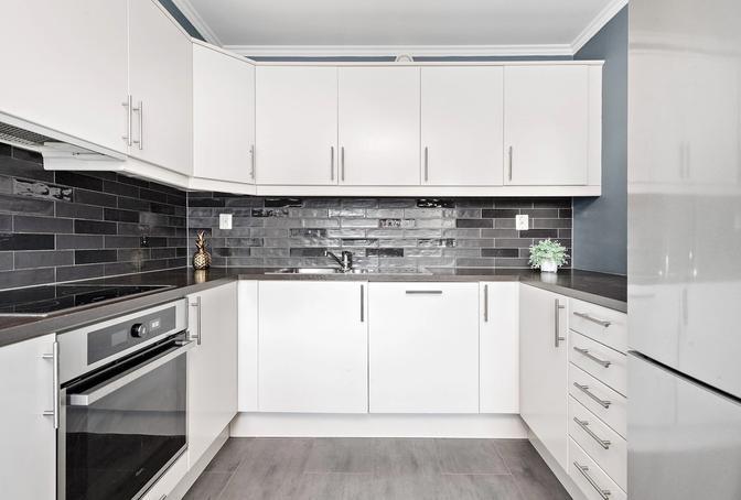 Kjøkkeninnredning fra Norema med hvite glatte fronter, laminat benkeplate og integrerte hvitevarer.