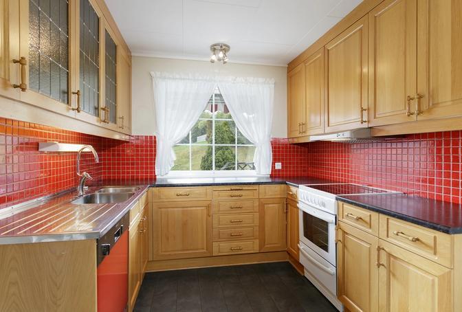 Kjøkkenet har innredning av eik med profilerte fronter, benk m/ dobbel vask og fliser på vegg over benk